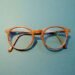 Spectacle frames with lenses on a teal background — dispensing accuracy and spectacle remakes in a UK independent optician practice.