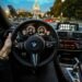 Driver's view through the windscreen of a city road at dusk with a hand on the steering wheel — driving and vision standards for UK independent optician practices.
