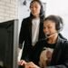Two customer support staff with headsets helping a client at a computer, illustrating practice management software onboarding and support